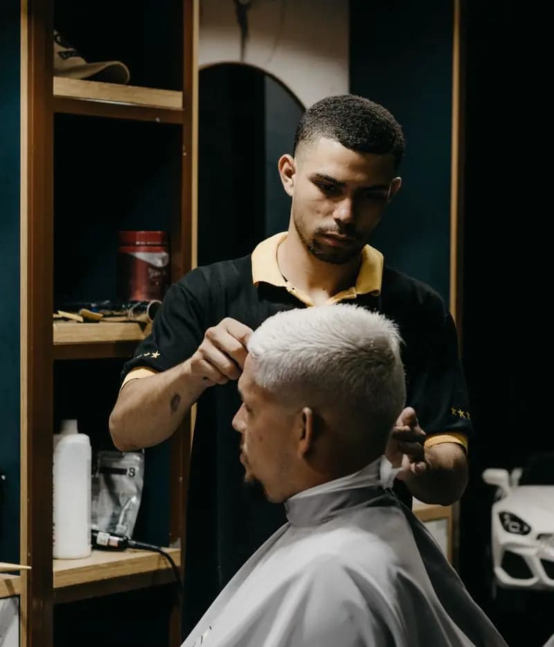 A barber trims the hair of a client sitting in the chair