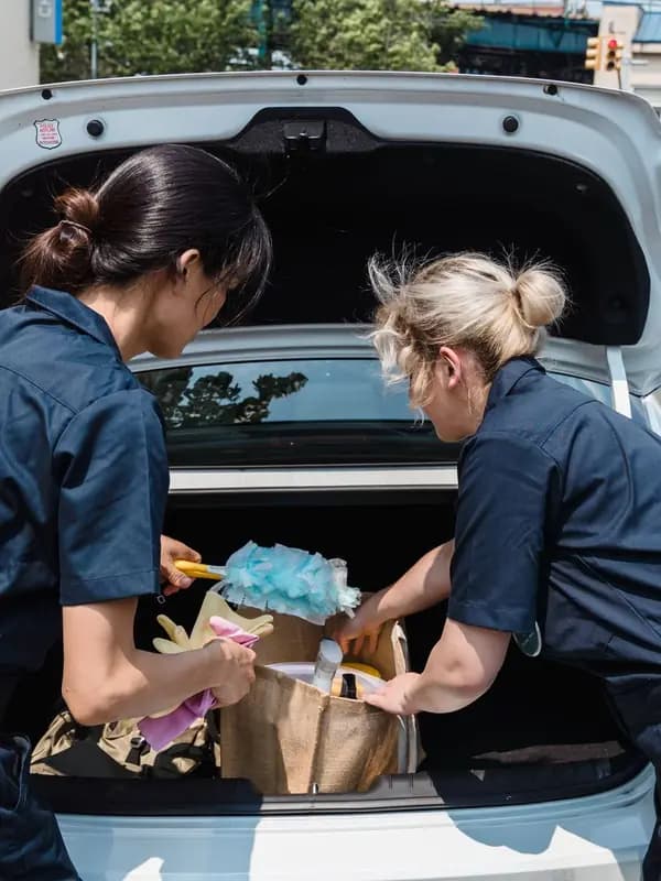 Two cleaners unload their supplies from a car