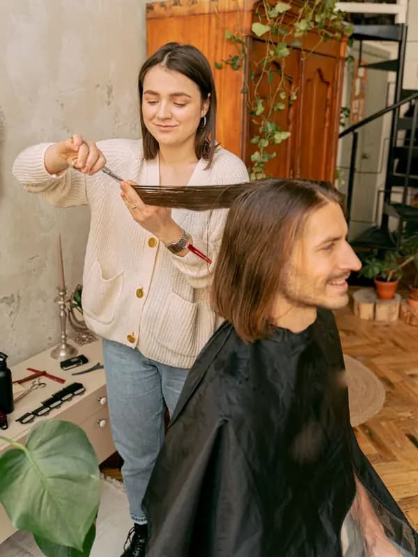 A stylist cuts a bearded man's hair in a salon